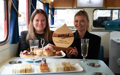 Two people holding their trophy inside a double decker bus with a three tier afternoon tea and two glasses of prosecco. Cake shop Brighton