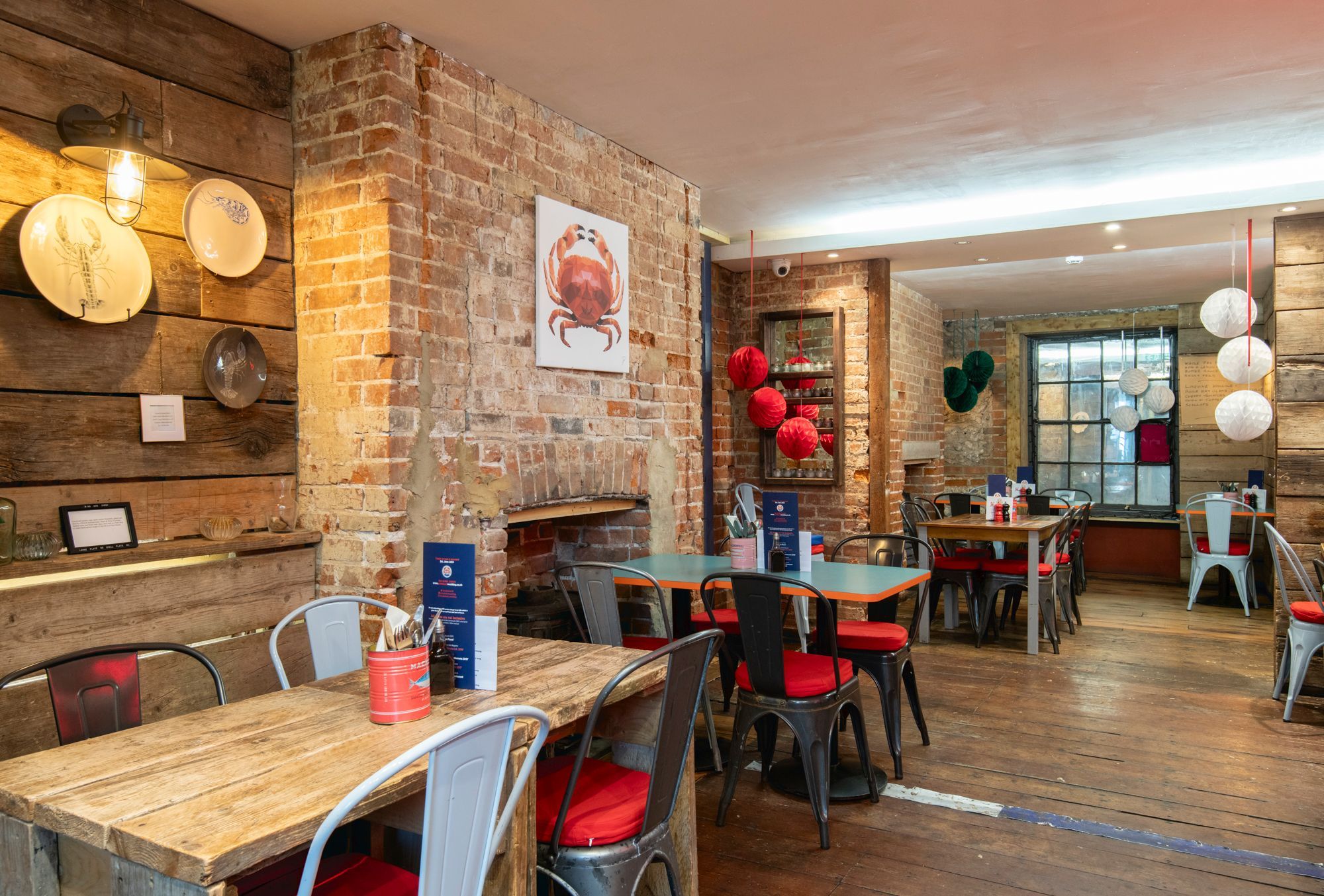 interior shot of the Crabshack. Wooden and brick walls, wooden tables and chairs with red covers.
