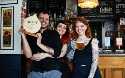 The team at The Geese in Hanover sat at the bar with the wooden BRAVO trophy with a beer.