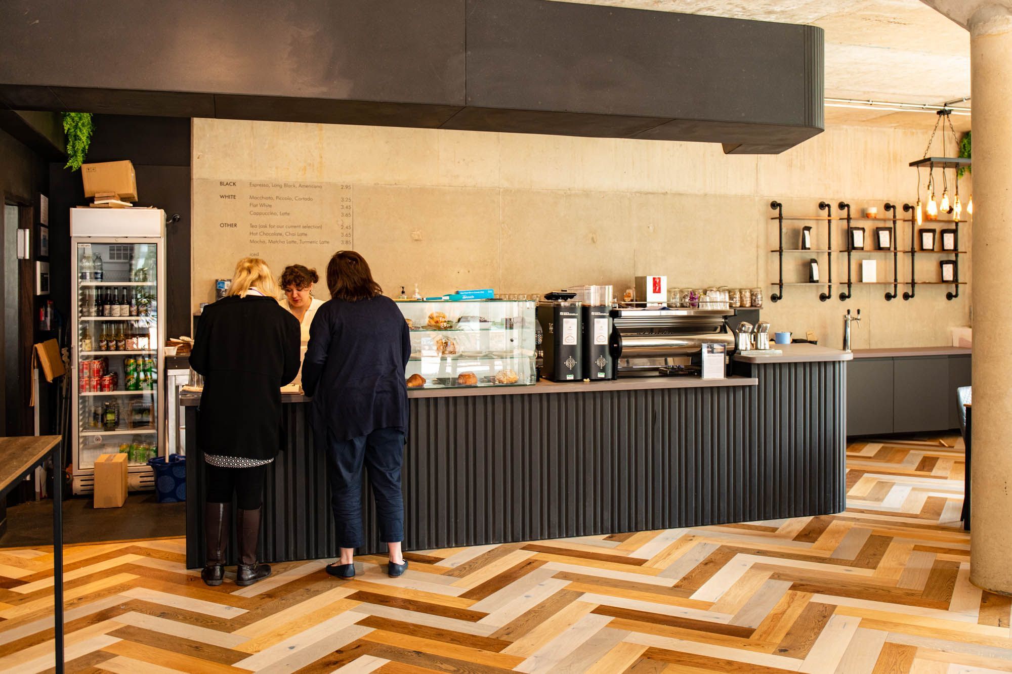 interior shot of the white cloud coffee, brown floor, black serving table, and two women ordering 