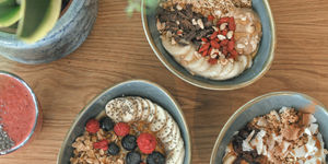 An overhead photo of bowls filled with Greek yoghurt and fresh fruit topped with Greek honey. Served in oval ceramic bowls with a blue glaze.