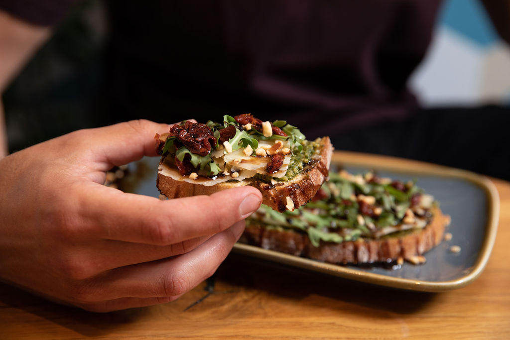 person holding a piece of delicious looking toast bread covered with cheese bits, cranberries, salad