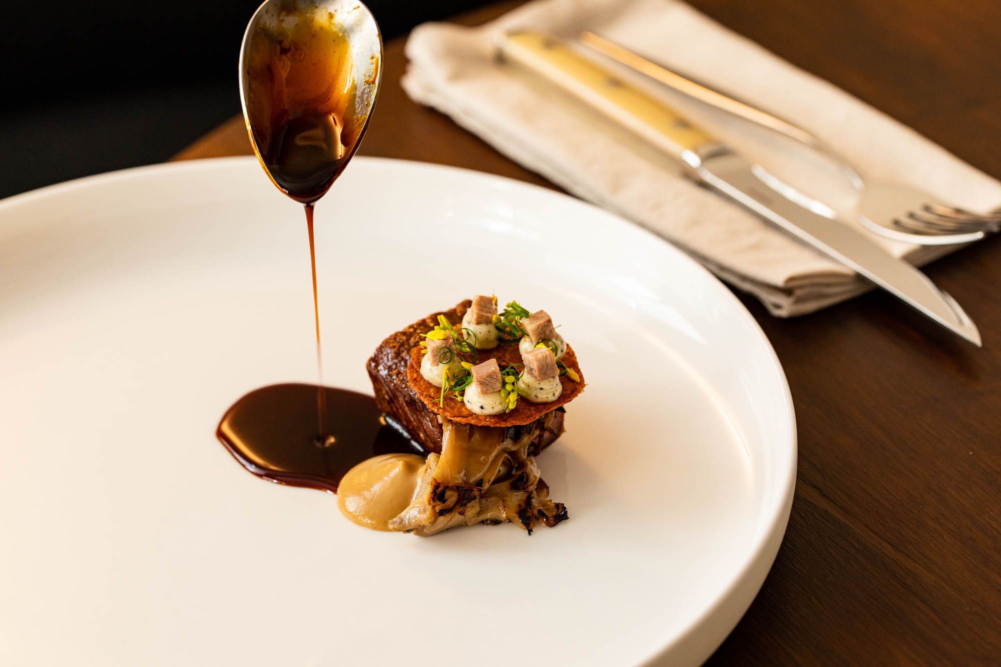 gravy dripping of spoon on the small dish served on the white plate, on the dark brown table