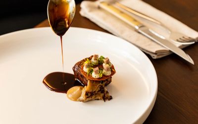 gravy dripping of spoon on the small dish served on the white plate, on the dark brown table. Part of the Fine Dining Brighton Guide