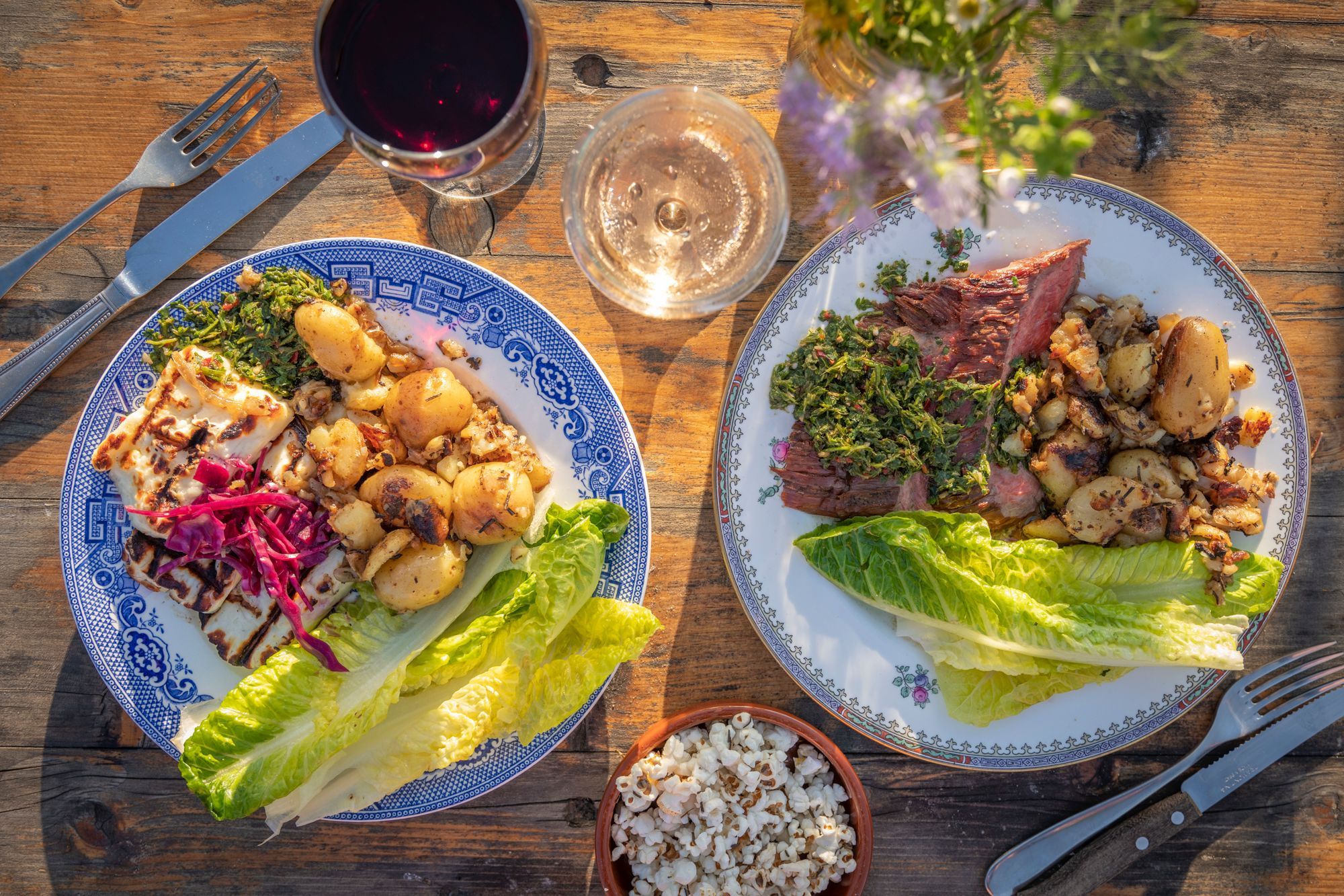 over head shot of two meal served at Woodfire Camping, one plate includes red meat with potatoes and salad leaves, other plate includes halloumi, potatoes and greens