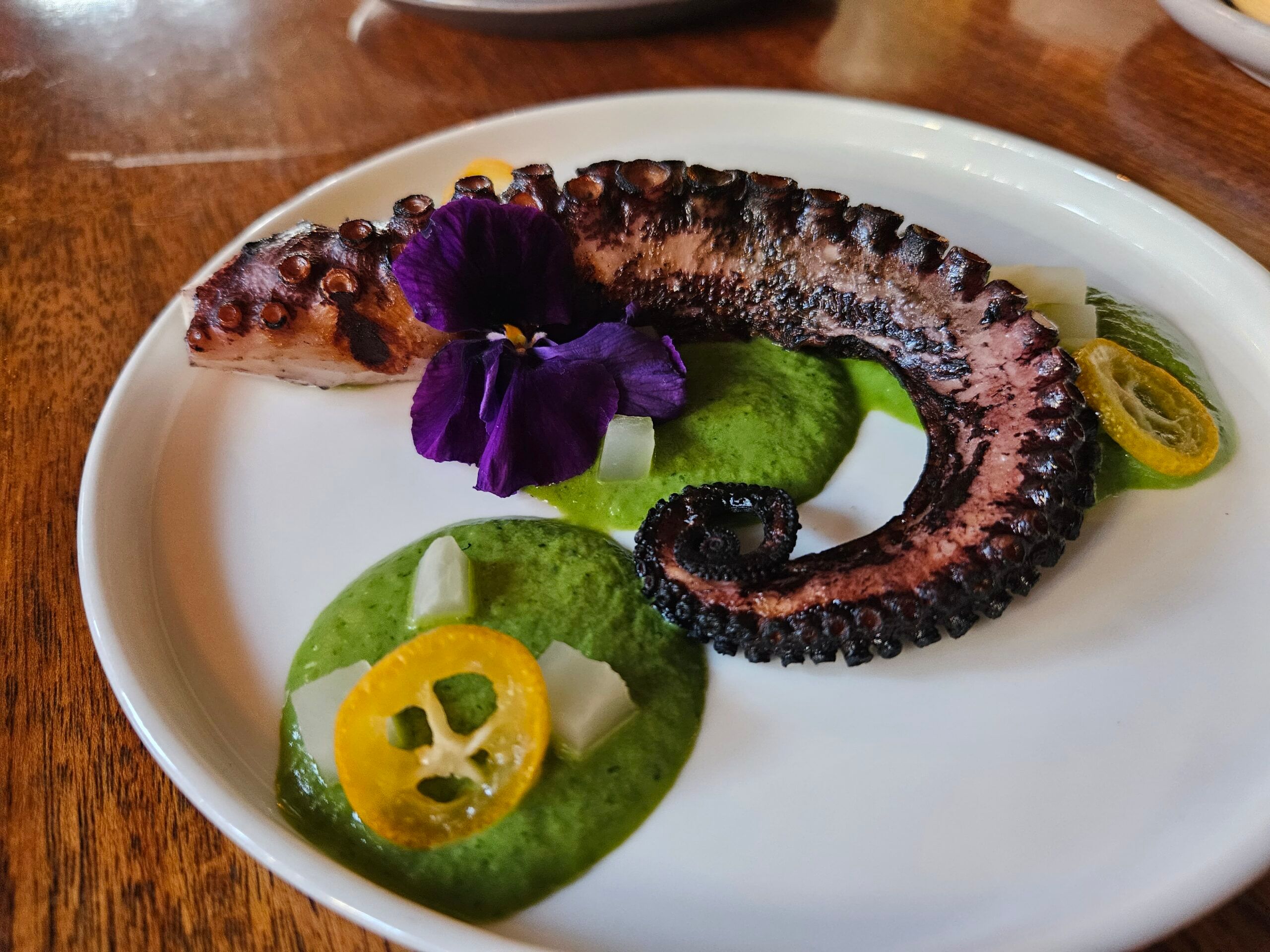 gorgeous purple octopus tentacle twirled atop a vibrant green edamame puree