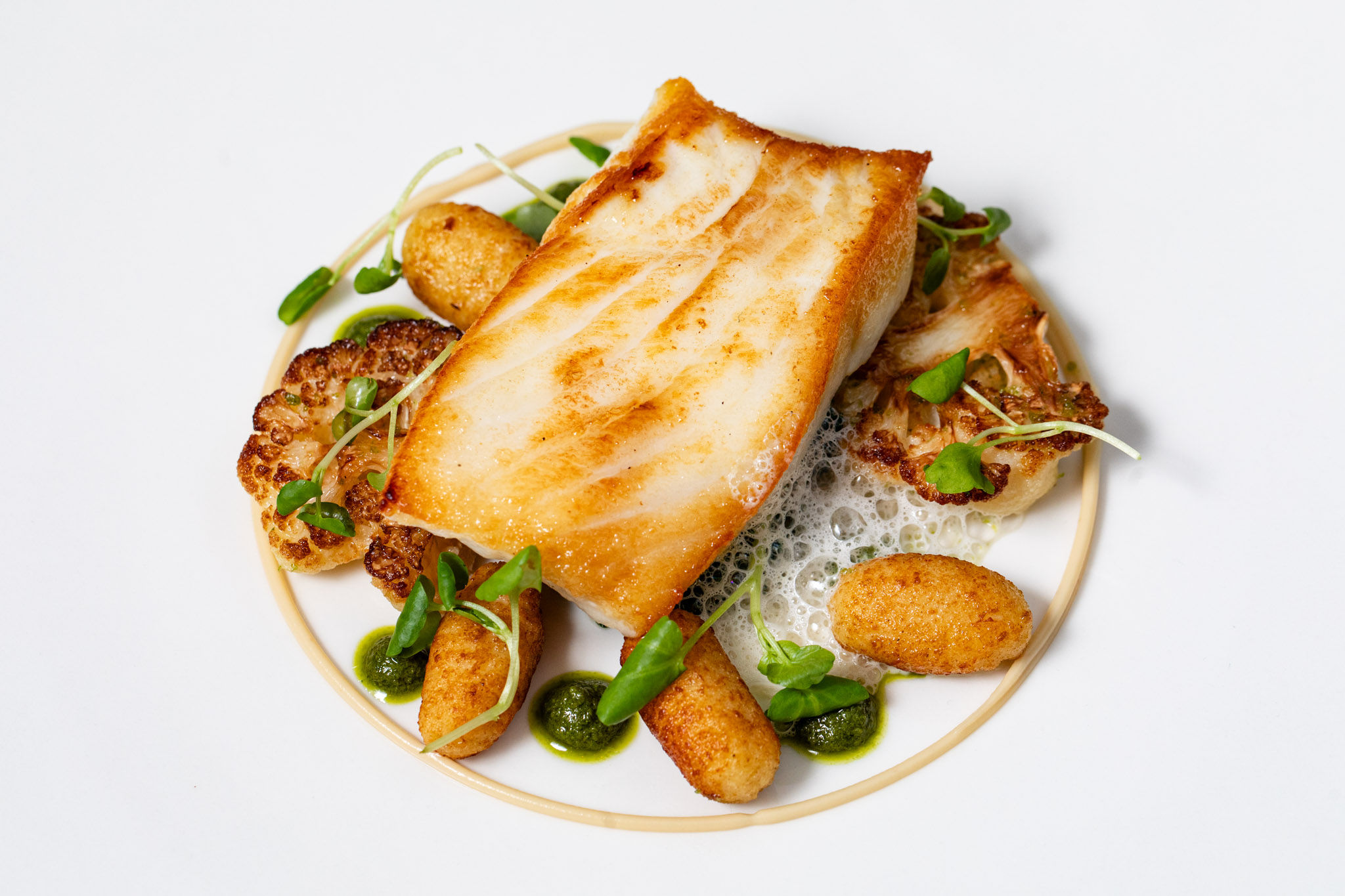 A plate of fish with garnishes and microgreens served in the centre of a white plate.