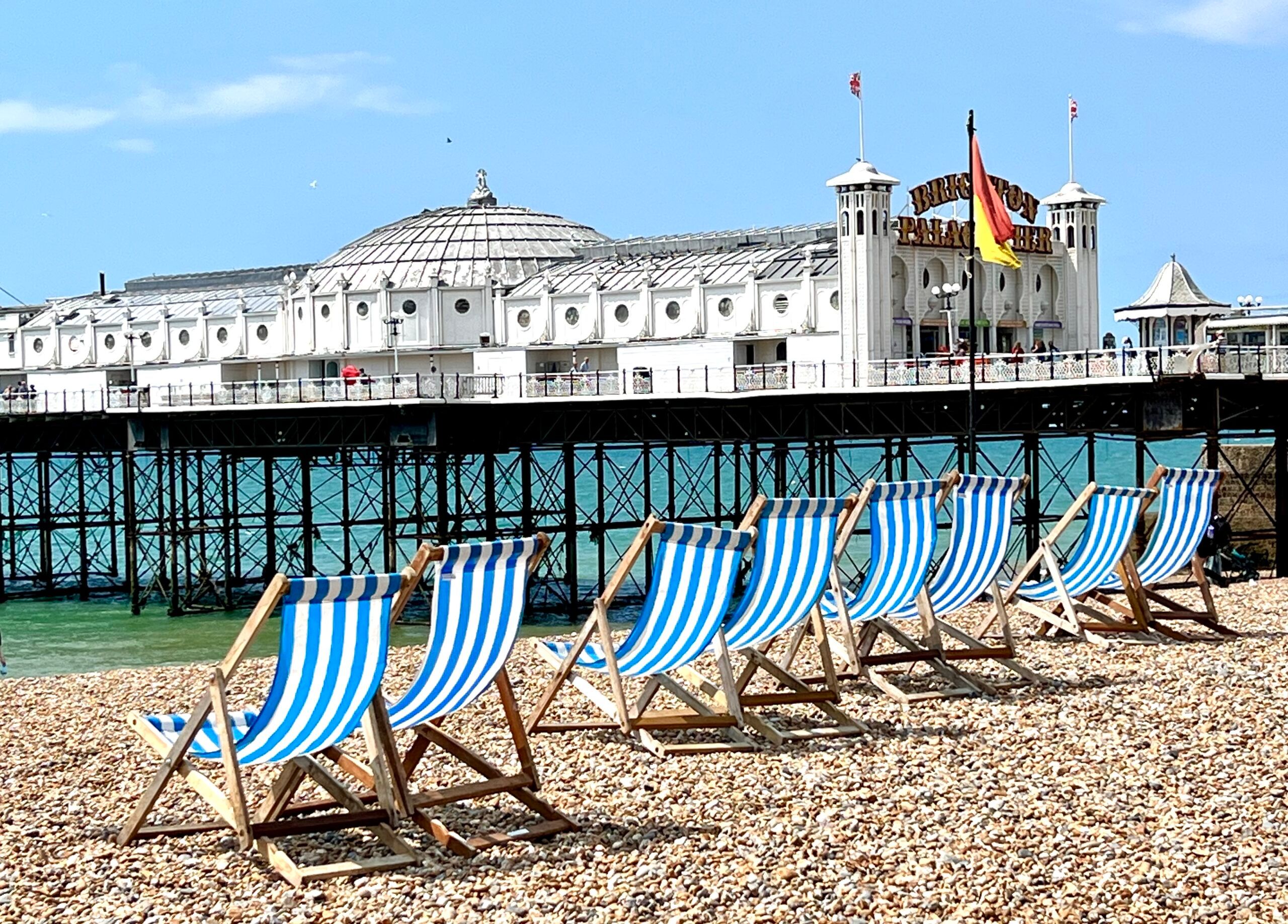 Deck chairs on the pebbles next to Brighton pier on a sunny day with a clear blue sky. Brighton Holiday