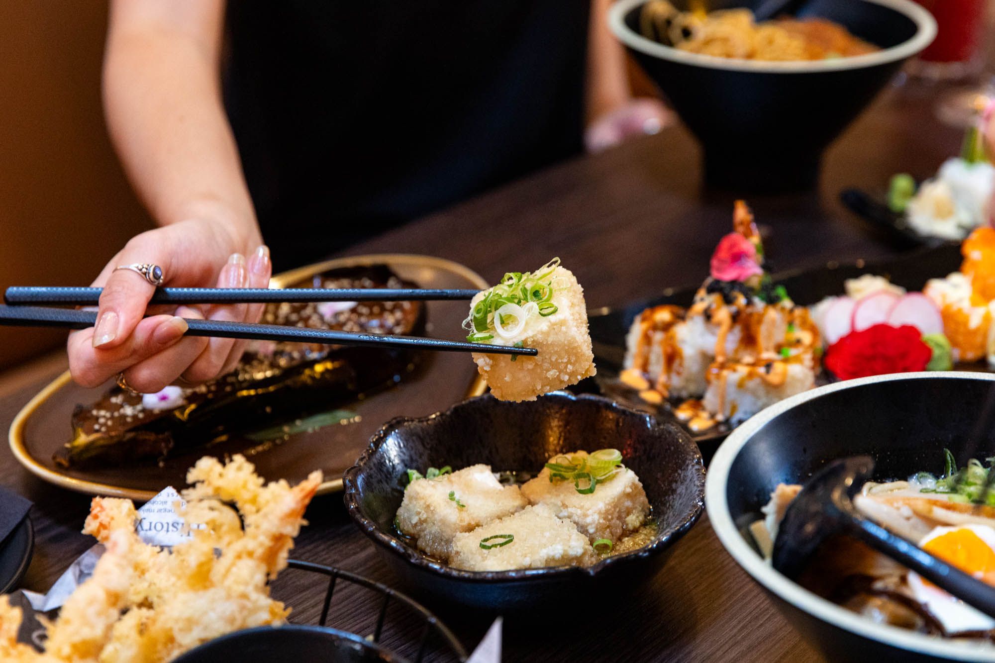 hands holding sushi with chop sticks above the table with Japanese dishes