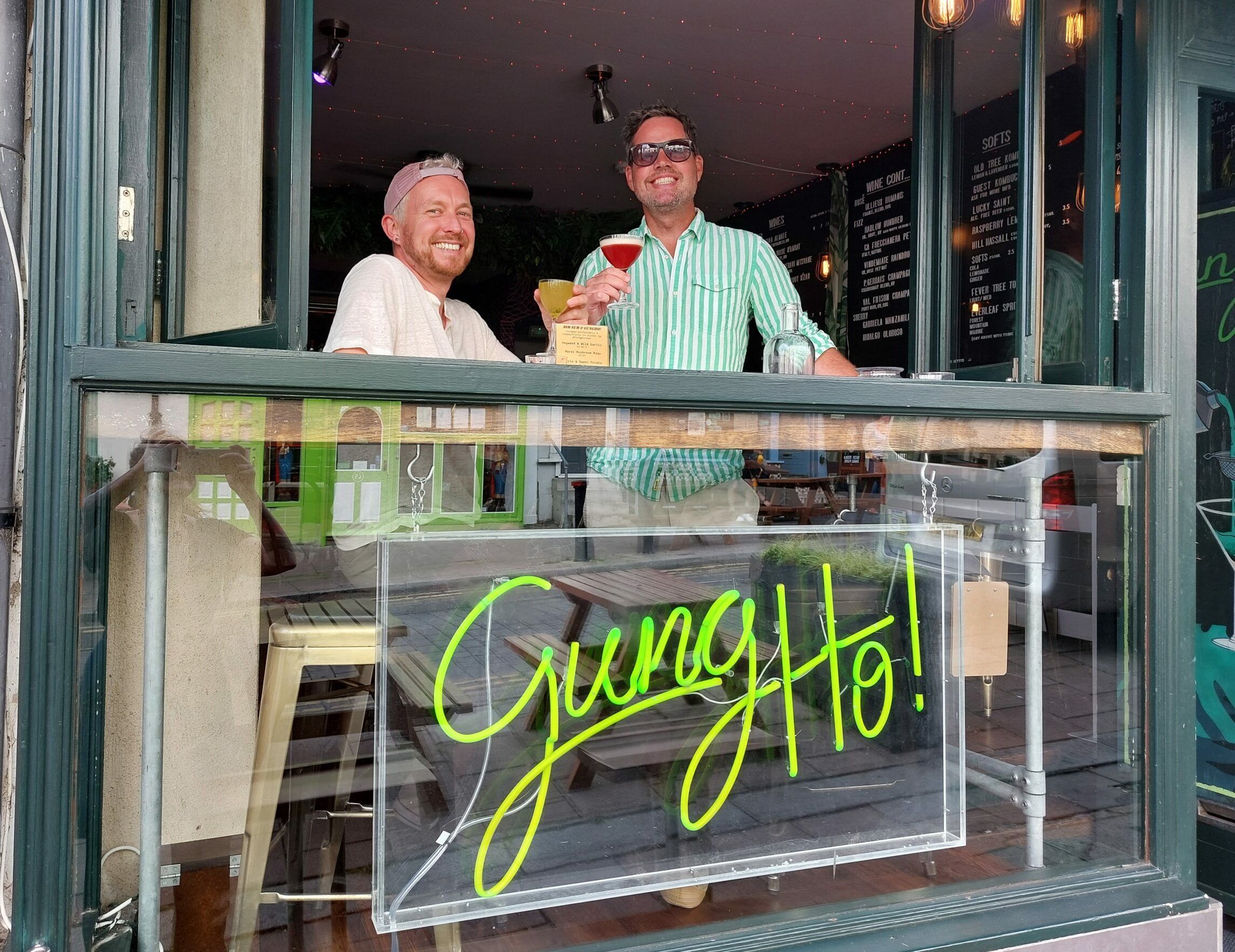 Torsten and Rhys standing at the window of GungHo bar and holding their cocktails