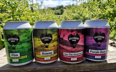 Ascension Cide Sussex Supplier of Cider. Pictured their four cans of cider against the backdrop of their orchards.