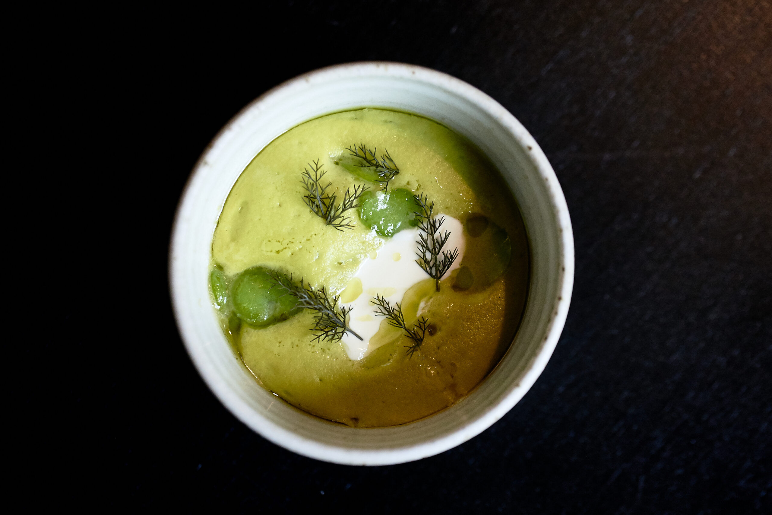 A green broad bean soup served in a small ceramic bowl on a black table for the four-course lunch at etch.