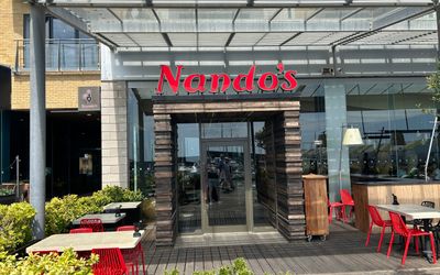 The facade of Nandos restaurant on Brighton Marina. Pictured red signage with glass building and terrace plants and tables