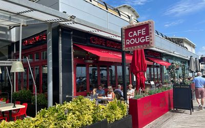 The facade of Cafe Rouge next to the backdrop of the blue sky. Showing terrace or alfresco dining at harbourside