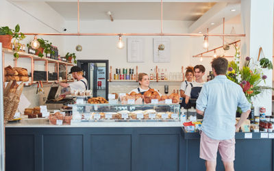 The Flour Pot Bakery in full swing. Smiling staff greeting customers and a shop front with all their artisan breads. Sussex Supplier Directory.