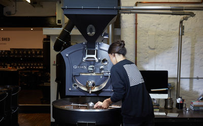 The Milk Shed coffee roaster in operation. Pictured a member of the team in dark colours operating the coffee roaster.