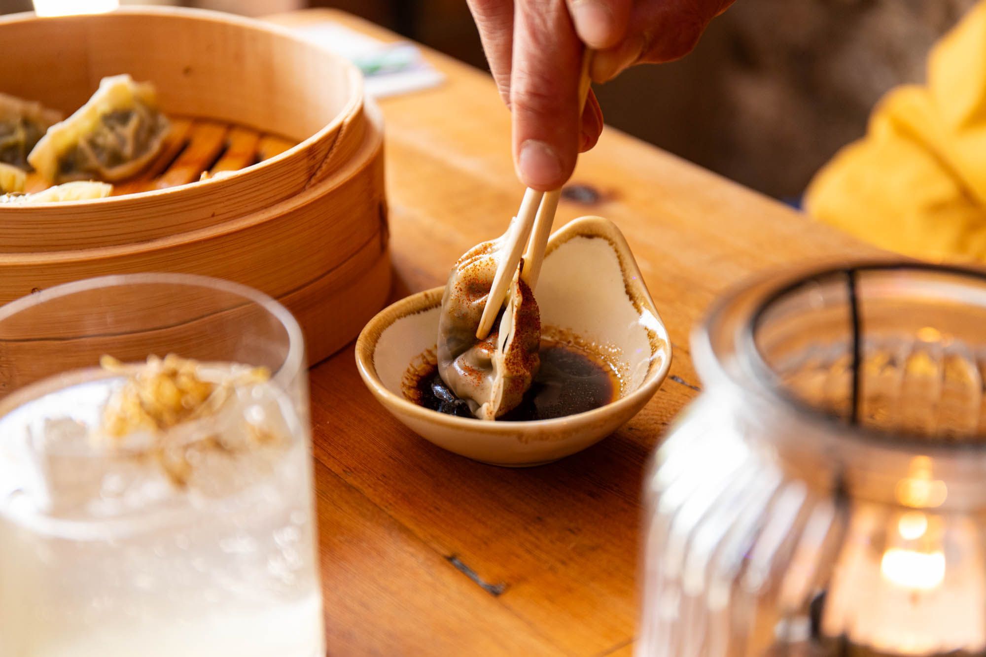 Person dipping dim sum with the chopsticks in the sauce. Dim sum and cocktails blog at the Gungho bar.