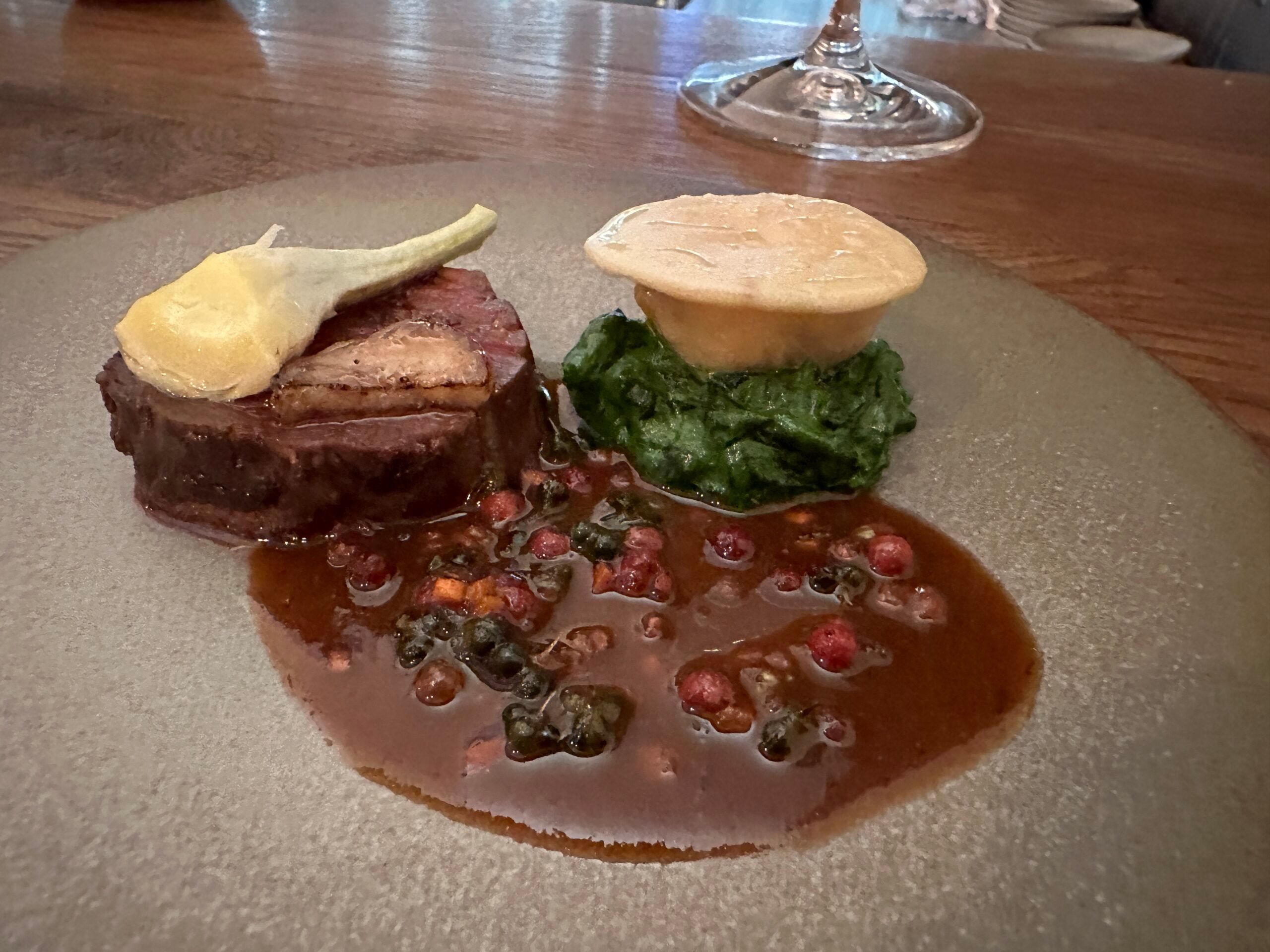 Beef dish with a rich sauce served on a grey plate with a glass in the background.