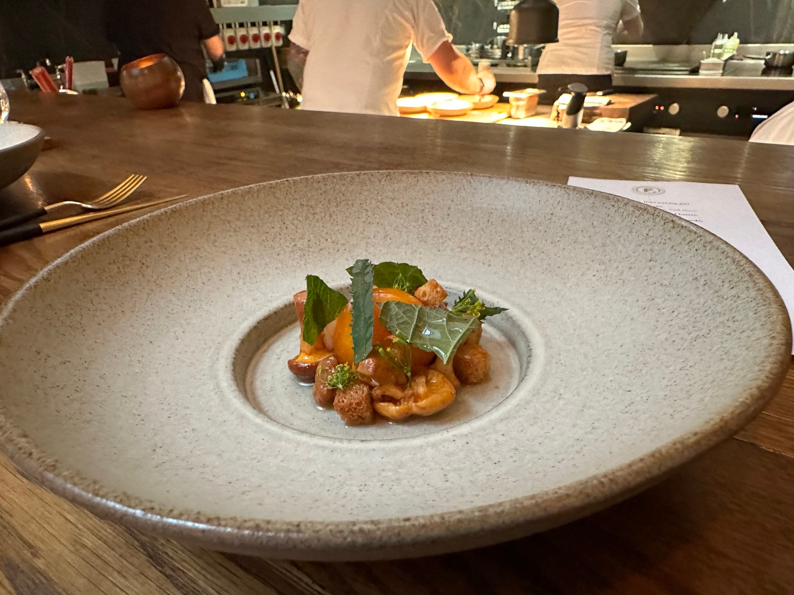 Girolles served on a large round plate with the kitchen of the restaurant in the background.