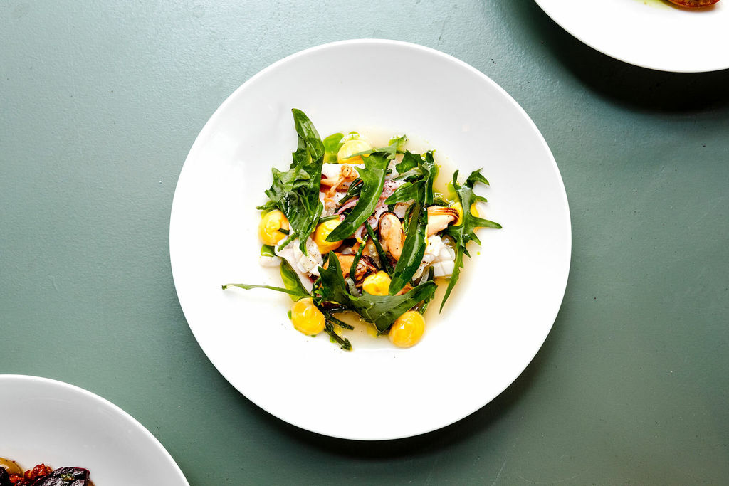 A white plate with pasta and rocket photographed on a pale green surface.