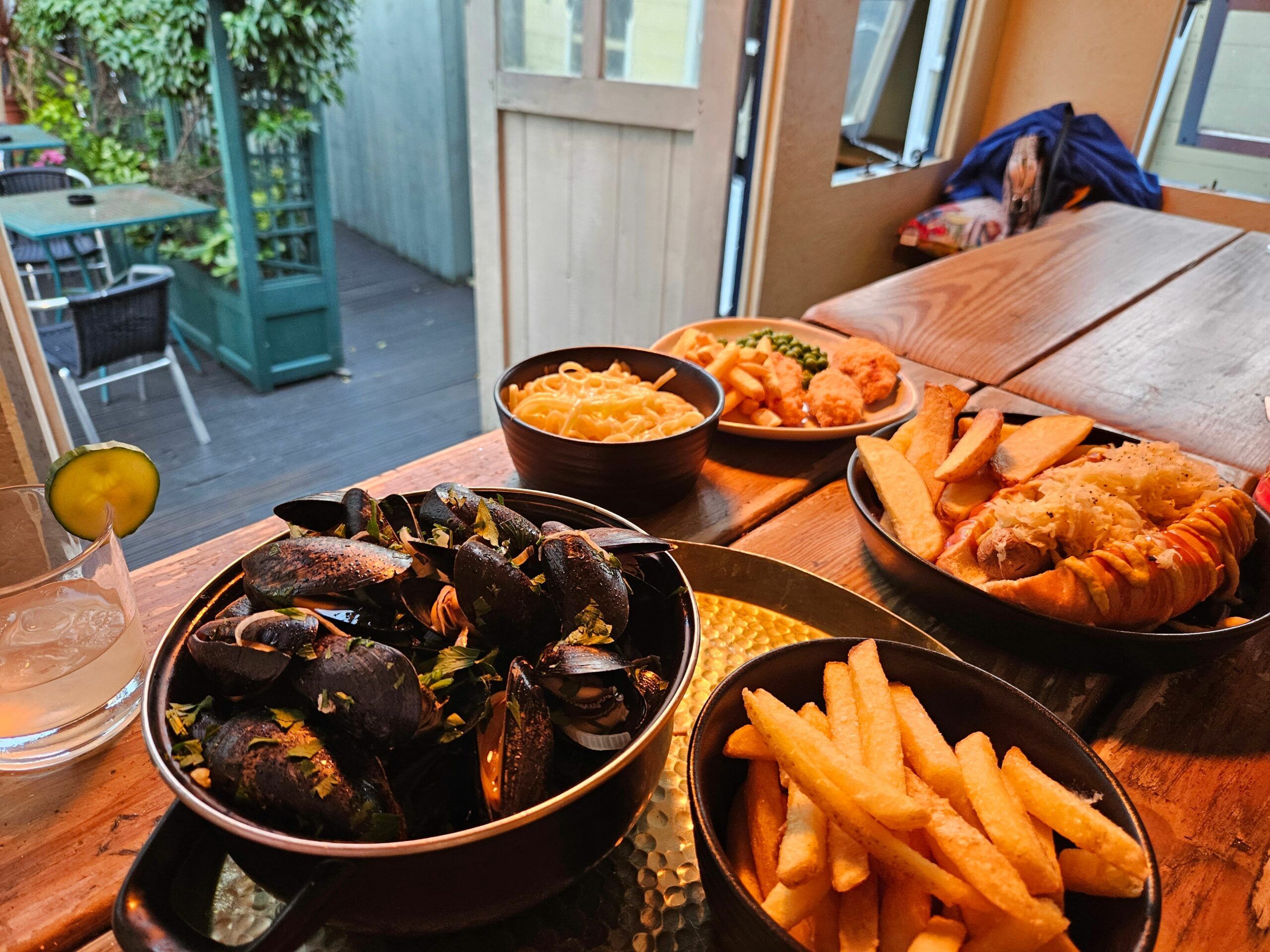 table laid out with 4 dishes including mussels, fries, pasta, fried chicken. Fantastic food