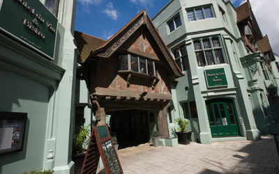 Exterior of a tudor style building. Green in colour with and exposed brick overhanging entrance.