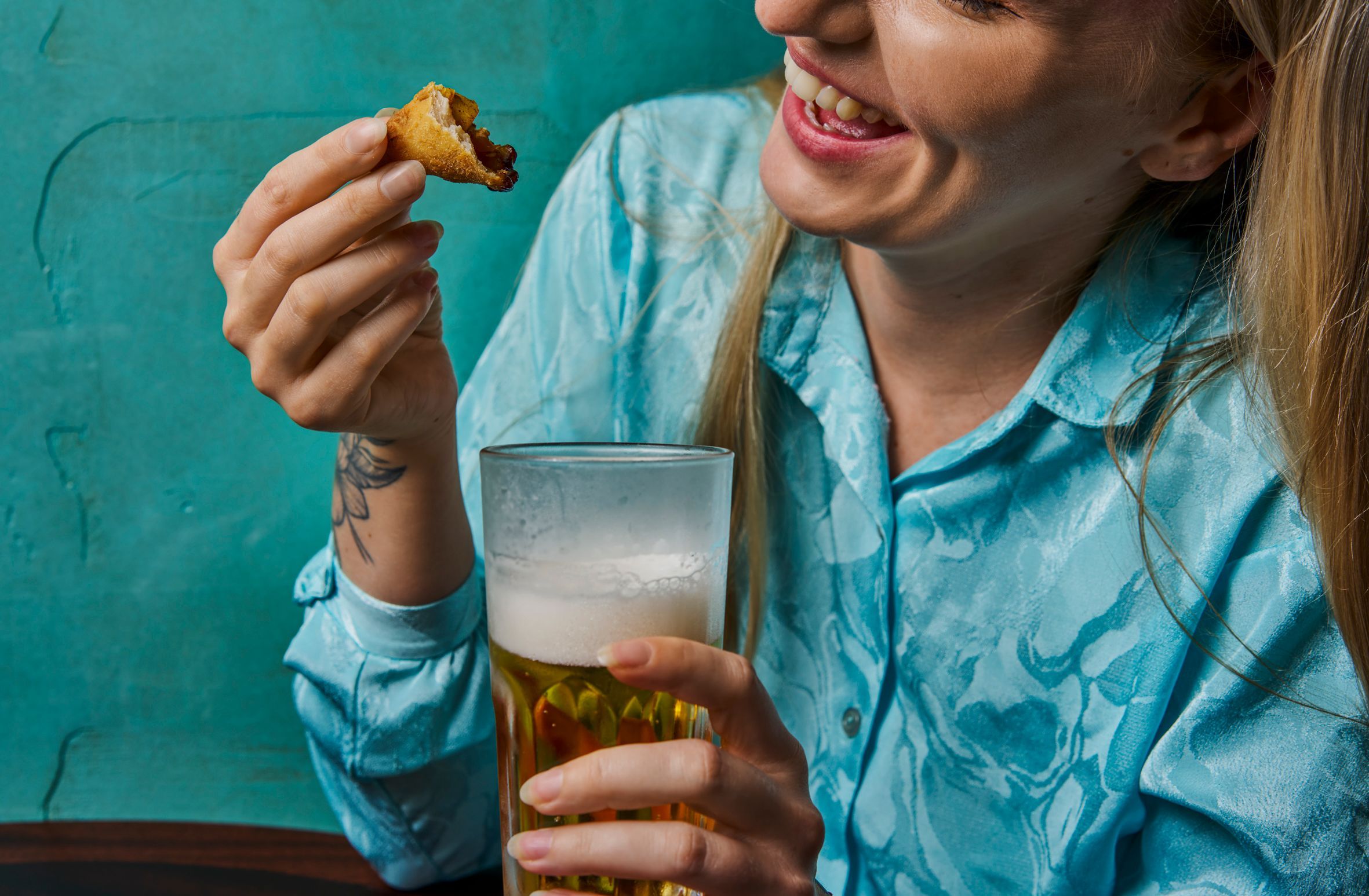 blonde woman in blue shirt having a beer and food 