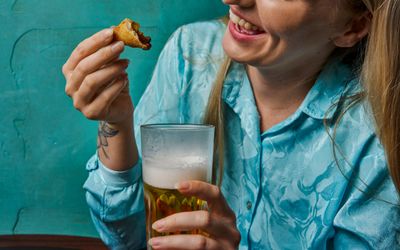 blonde woman in blue shirt having a beer and food