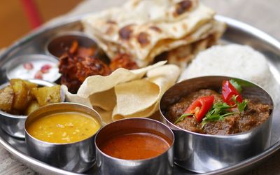 Thai served in metal pots on a metal tray with curries, naan and chutneys.