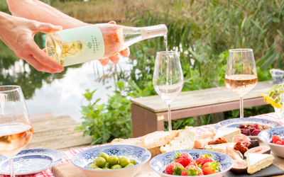 Wine being poured into a glass next to a lake with fresh fruit and a bowl of olives.