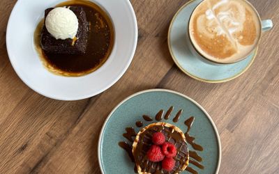 over head shot of two desserts including sticky toffee pudding and chocolate torte topped with fresh raspberries and lashings of caramel sauce with flat white coffee
