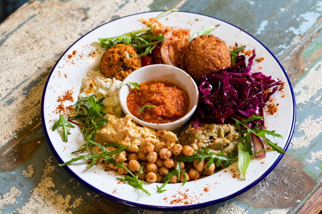 vegan restaurants in Brighton. a plate of middle eastern food including houmous, red cabbage, falafel and sald presented on a white plate on a wooden table.