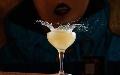 A cocktail with an ice cube being splashed into it.