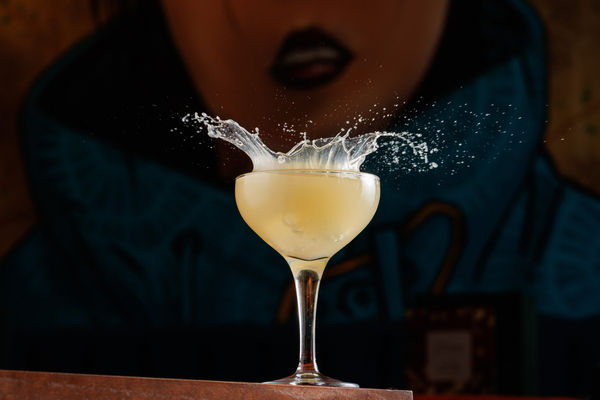 A cocktail with an ice cube being splashed into it.