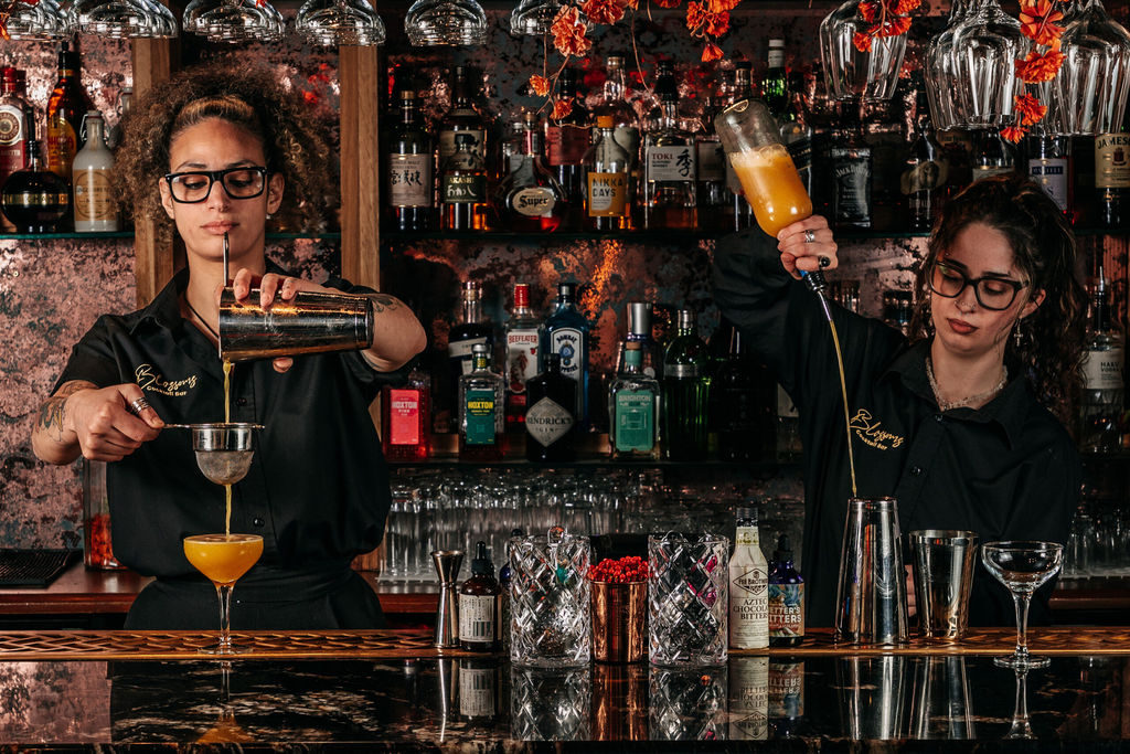 Two mixologists preparing cocktails behind the bar at Blossoms Brighton.