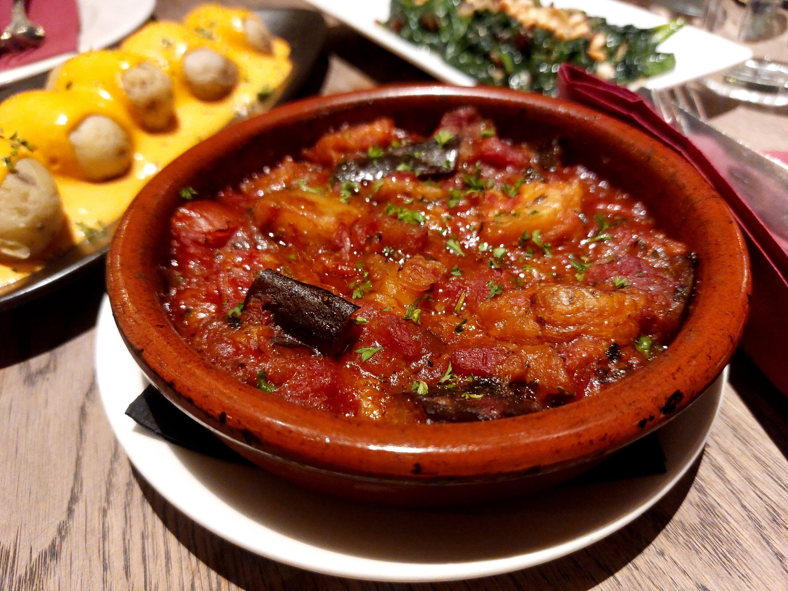 A terracotta bowl of tapas with plates of tapas in the background. Vegan tapas experience blog