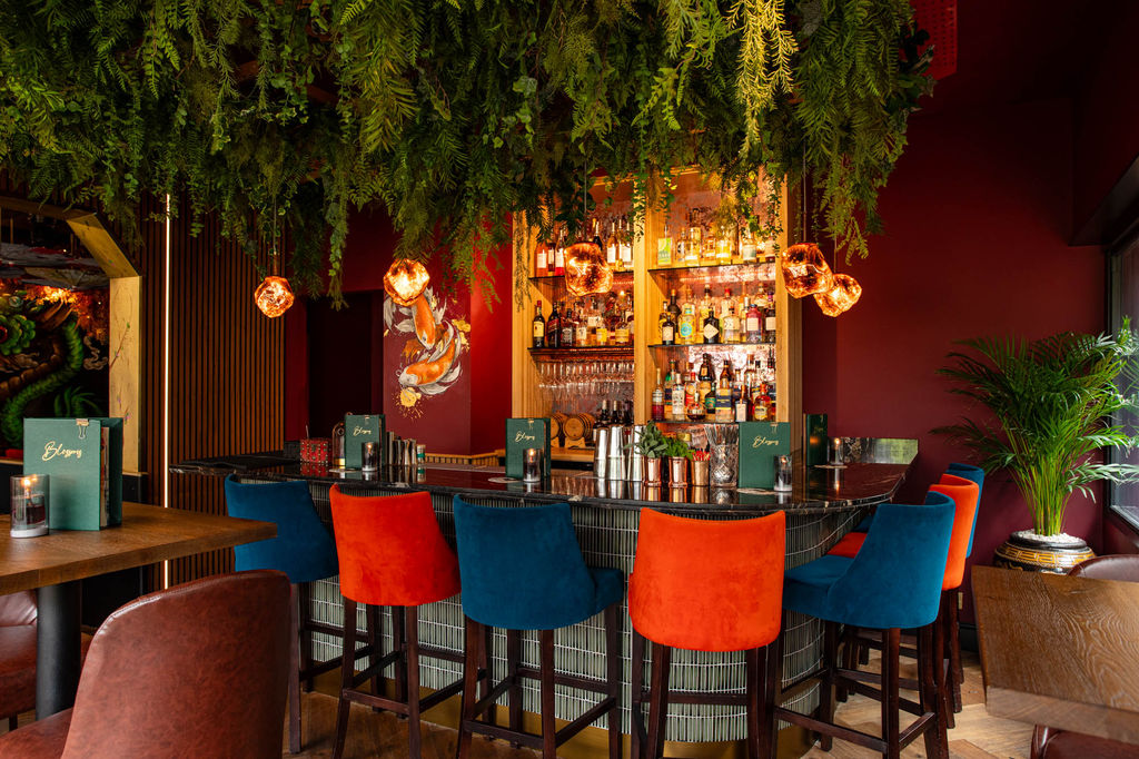 Interior photo of the Krimson Coi private room with orange and blue bar stools at the bar area and green foliage hanging from the ceiling.