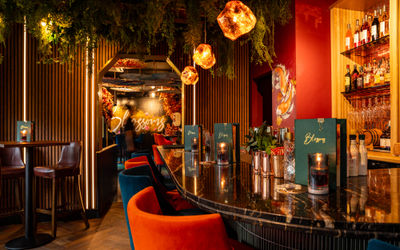 An ambient lit room with bar stools a the bar and green menus sat on the bar.