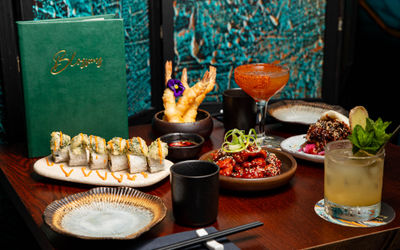Plates and bowls of sushi, snacks and cocktails photographed against a blue backdrop.