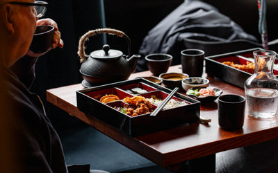 Tea and bento box at Blossoms A table with a bento box and black tea pot with black cups.