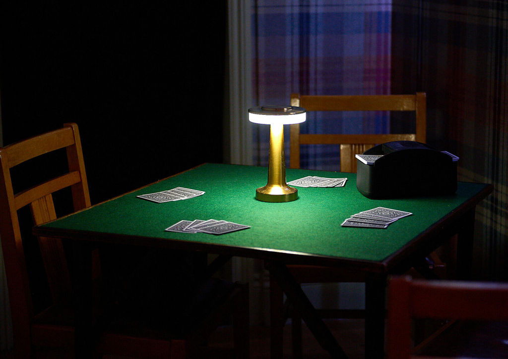 A bridge table with playing cards with a lamp in a dark lit room.