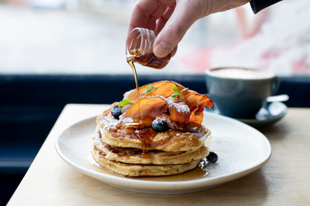 Syrup being poured over a stack of panckes
