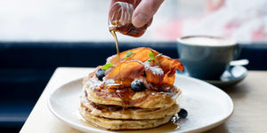 Syrup being poured over a stack of panckes