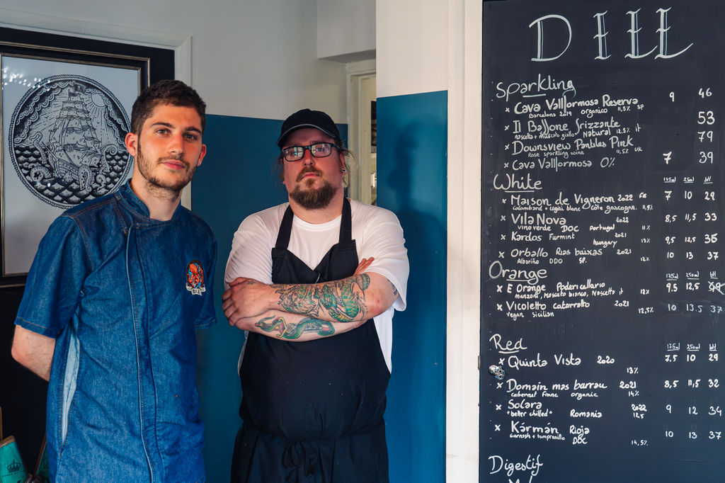 Dill restaurant in Lewes. Chef and proprietor posing for a picture with a blue background, white walls and a black chalk board.