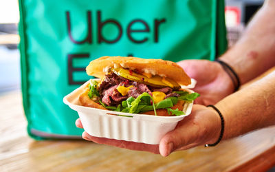 A sandwich being held in front of an Uber Eats delivery box.