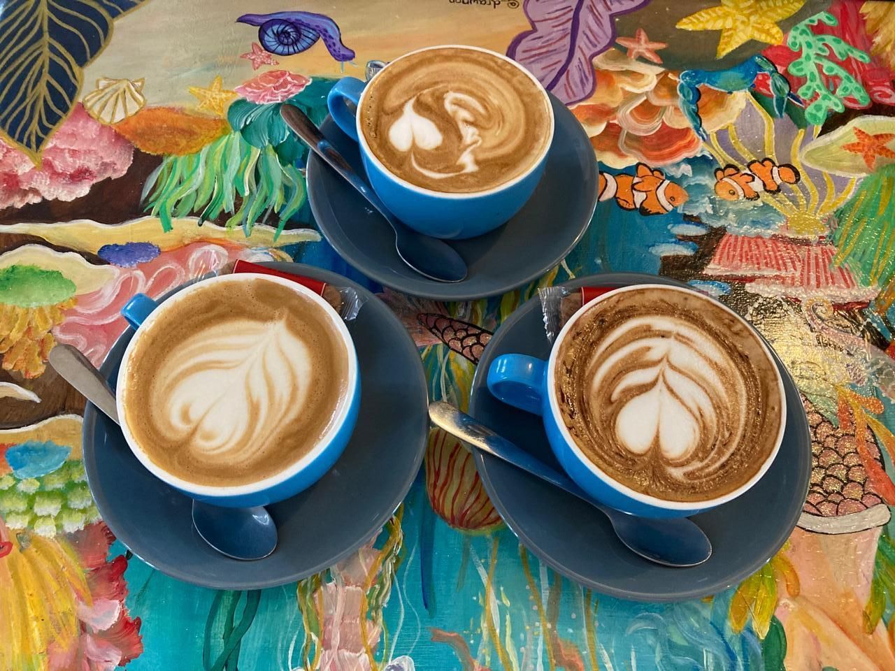 three flat white coffees on the colourful table at Arcobaleno