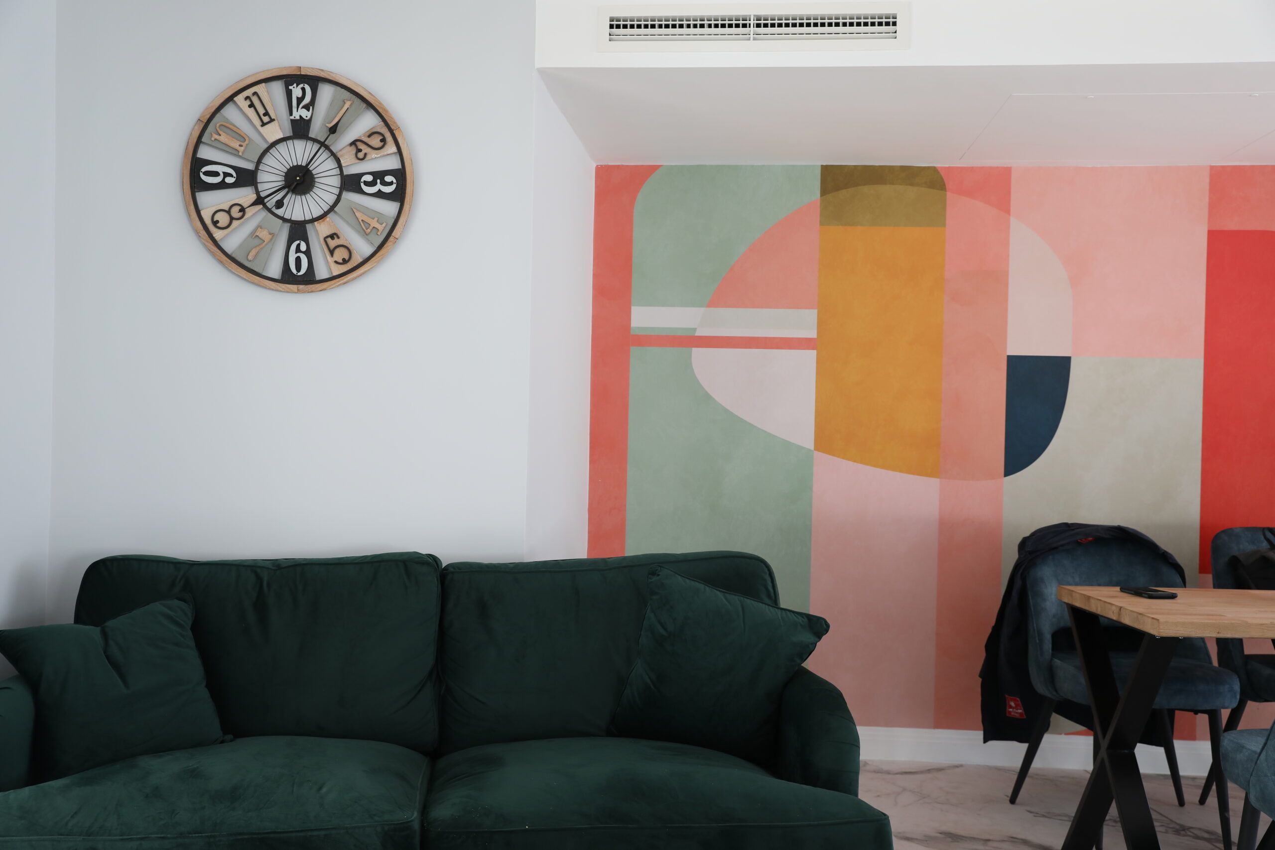 Relaxed vibes. Simple artwork next to a dark green couch with a clock on the wall. 
