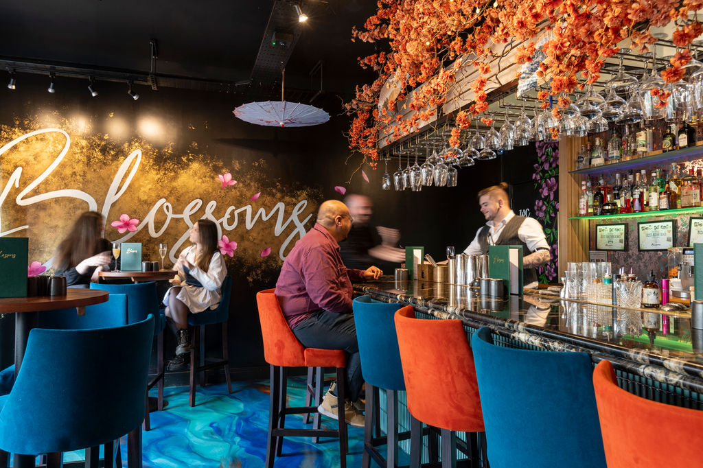 Blossoms Cocktail Bar located in Dolphin Square in central Brighton. Pictured a vibrant and lively interior with brightly coloured stools, flowers and customers enjoying their cocktail experience. Blossoms is featured on the Restaurants Brighton guide.