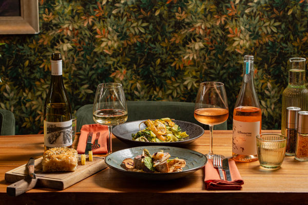 A table with food and glasses of wine against a leaf printed wallpaper