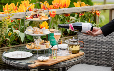 An afternoon tea set up on a table outside with orange tulips in the background and a glass of sparkling wine being poured. Alfresco Dining in Sussex. Best lunches in Brighton and Sussex